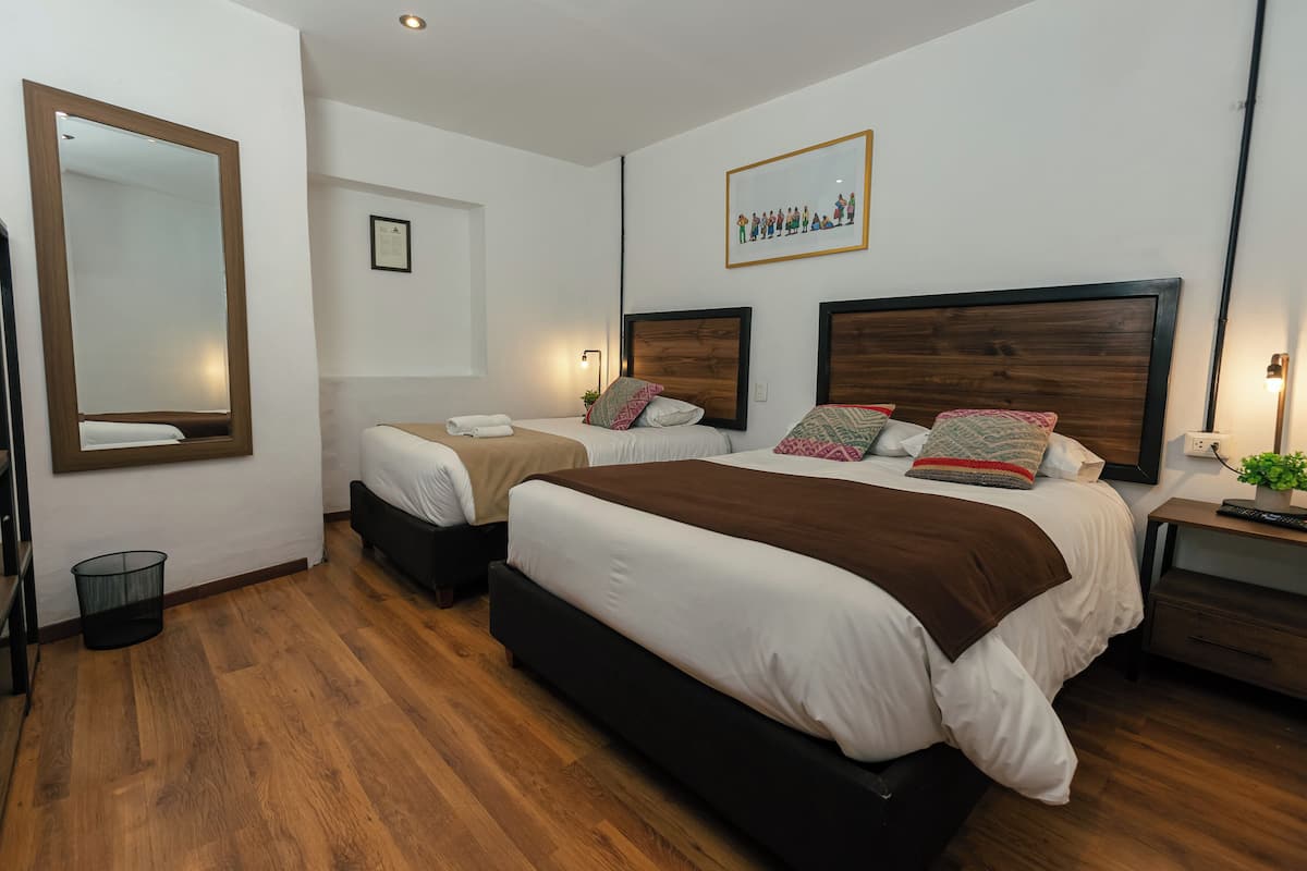 Ein Hotelzimmer mit zwei Betten, einem großen Spiegel, einem gerahmten Bild an der Wand und einer kleinen Pflanze auf dem Nachttisch.