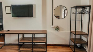 A room with a wooden table, a wall-mounted TV, a mirror, a hanging clothes rack, and a small potted plant. - HOSTAL MARIA ANGOLA CUSCO (Cusco)