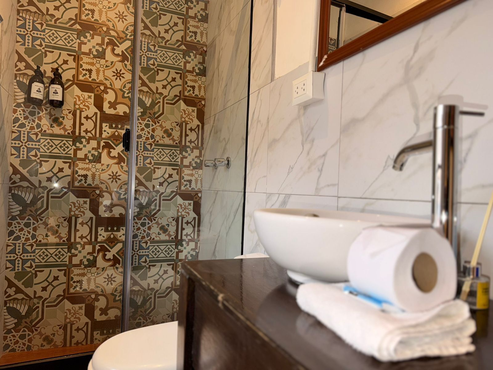 Une salle de bain avec des carreaux décorés, un lavabo blanc, un miroir et des toilettes.