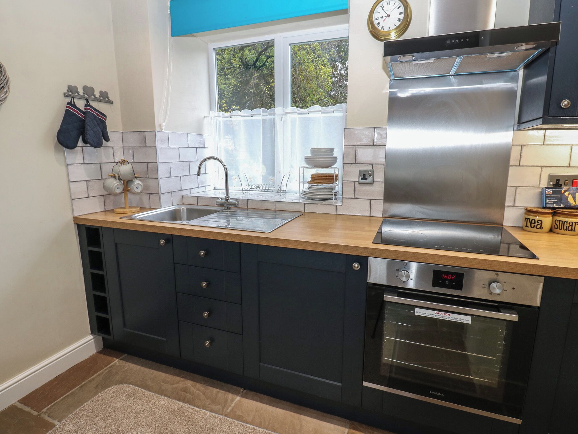 A modern kitchen with a stainless steel range hood, a built-in oven, and a double sink.