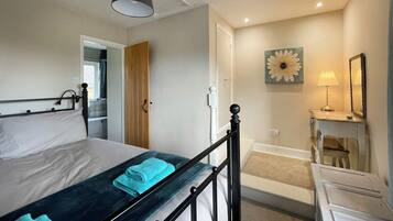 A bedroom with a bed, a bedside table with a lamp, a mirror, and a wall with a flower painting.