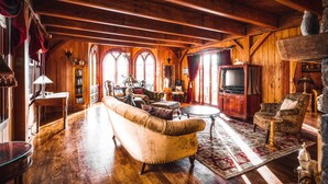 A cozy, rustic living room with wooden beams, a large sofa, a television, and a fireplace.