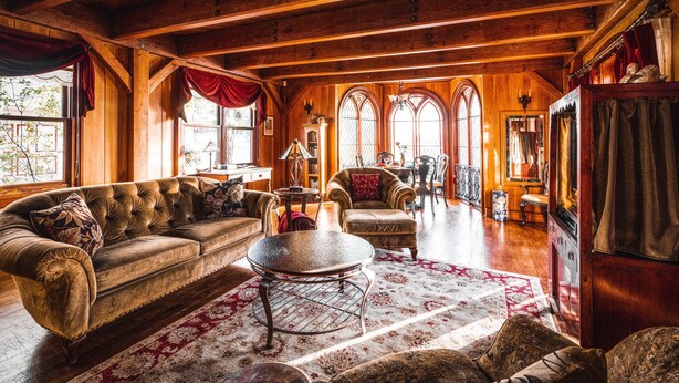 A spacious living room with a wooden ceiling, a large cushioned sofa, a round coffee table, and a fireplace.