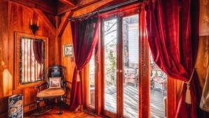 A wooden interior with a chair, a door with red curtains, and a view of the outside.