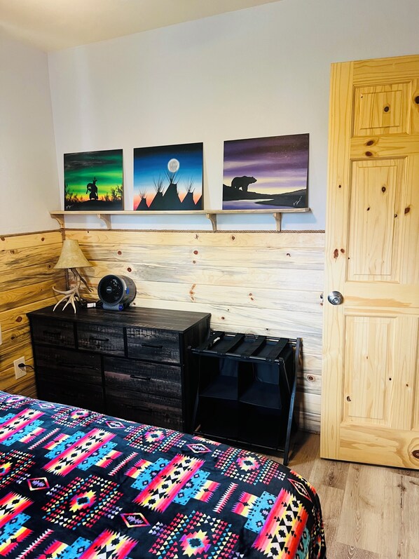Quarto com cama, penteadeira, abajur e três quadros na parede.