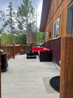 A wooden deck with outdoor furniture, a covered umbrella, and a view of trees.