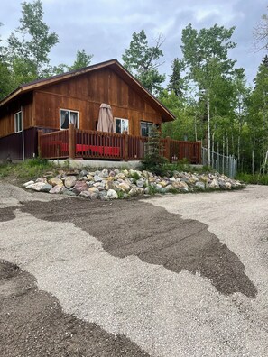 A wooden cabin with a gravel driveway, a wooden fence, and a stone garden.