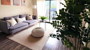 Ein modernes Wohnzimmer mit einem grauen Sofa, einem runden Hocker und einer großen Pflanze.