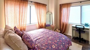 Ein Schlafzimmer mit Bett, Vorhängen, Deckenventilator, Schreibtisch mit Stuhl und Fenster.