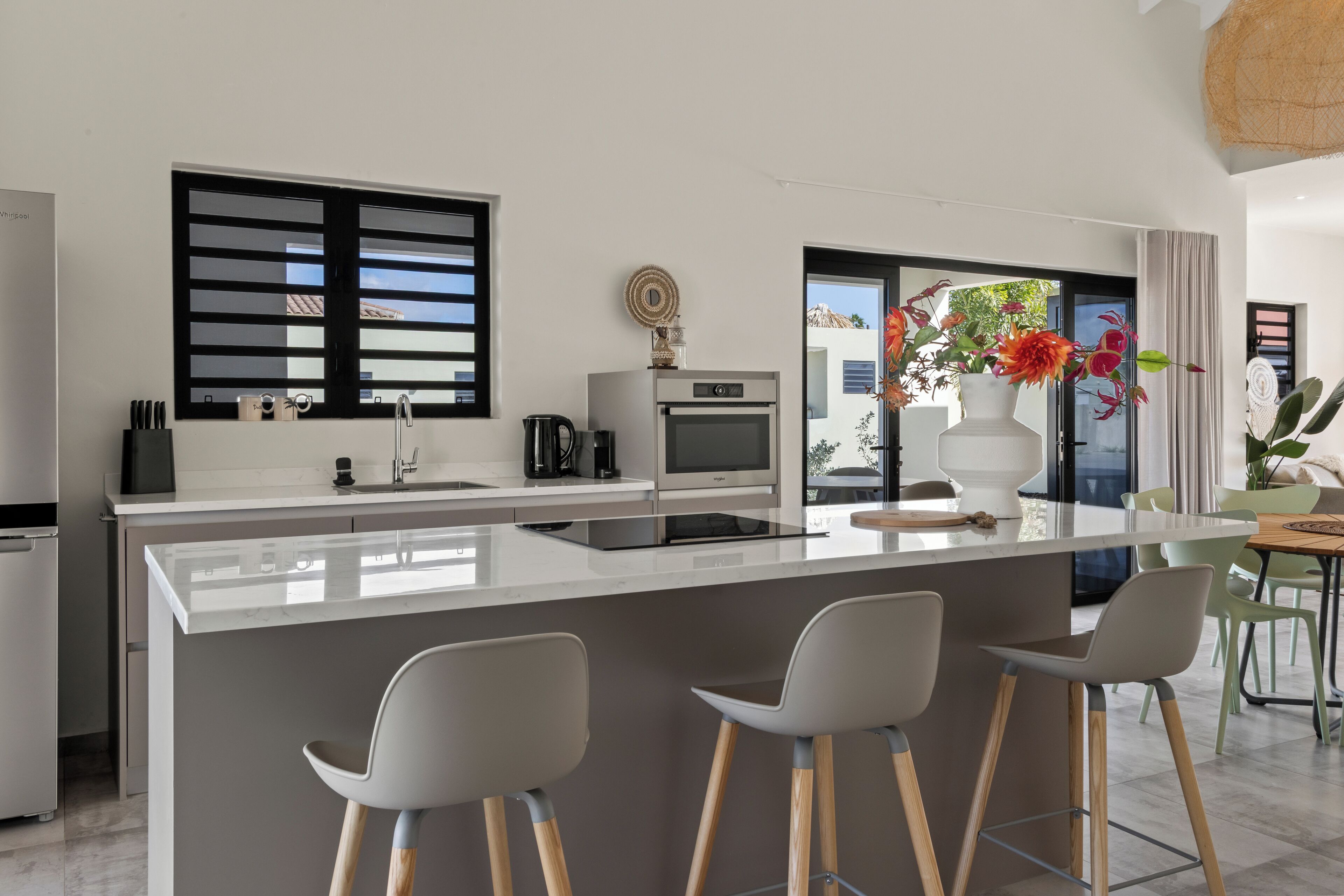 Une cuisine moderne dotée d’un îlot central, de tabourets de bar et offrant une vue sur l’extérieur.