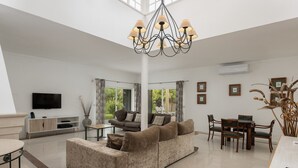 Uma sala de estar espaçosa, com um sofá grande, uma mesa de jantar e um candelabro.