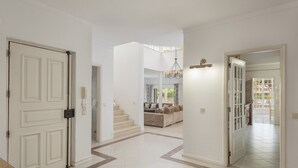 Um corredor espaçoso com paredes brancas, soalho em azulejos e escadas que levam a uma área de estar.