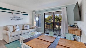 Un salon comprenant un canapé, une table basse et un coin repas avec des chaises et une table. Une porte-fenêtre coulissante donne accès à une terrasse extérieure équipée de chaises.