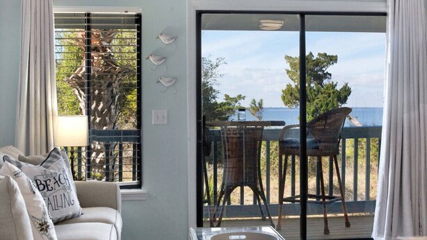 Une chambre avec vue sur la mer, un balcon avec des chaises et une fenêtre avec une cage à oiseaux.