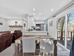 A modern kitchen with stainless steel appliances, a dining area with a wooden table and leather chairs, and a large sliding glass door leading to a deck. - Aspen Hideaway – Modern 2BR/2BA Condo Steps from Giant Steps Lifts (Brian Head)