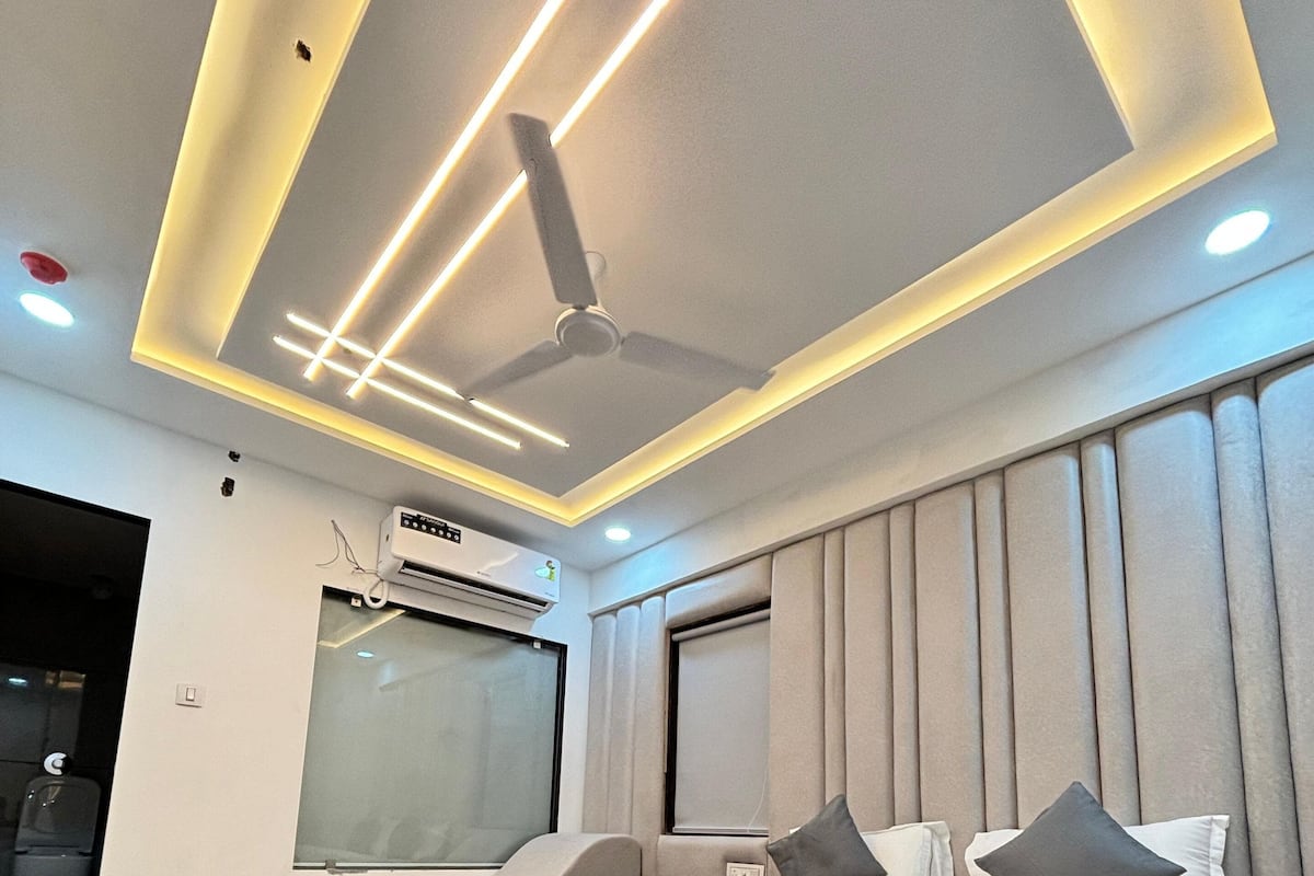 A modern bedroom with a large bed, a ceiling fan, recessed lighting, and a window with blinds.