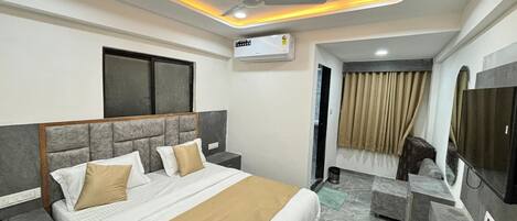 A hotel room with a bed, a television, a ceiling fan, and an air conditioning unit.