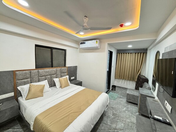 A hotel room with a bed, a television, a ceiling fan, and an air conditioning unit. - Hotel Sun Pride (Ahmedabad)