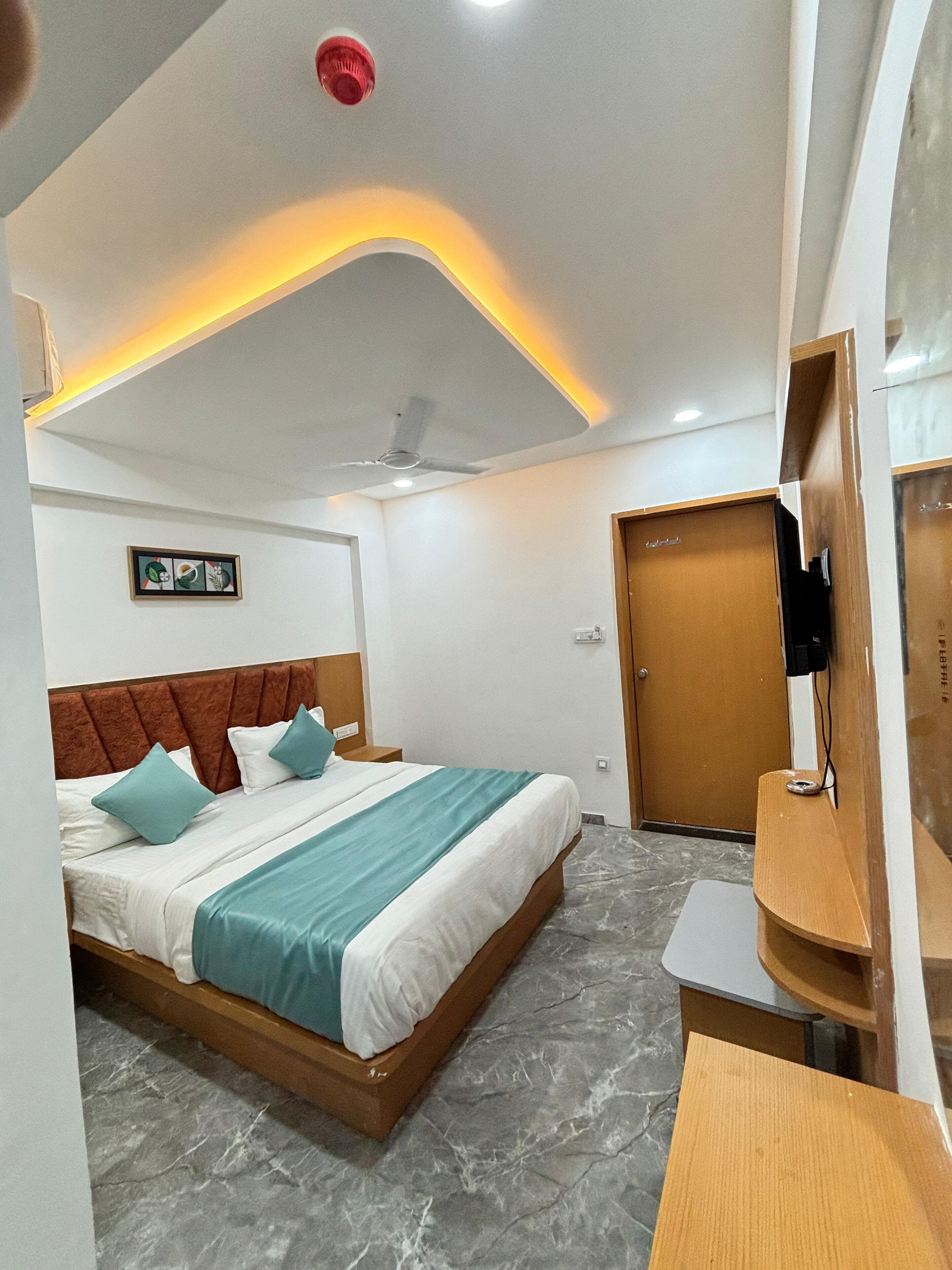 A hotel room with a bed, a ceiling fan, a door, and a small table.