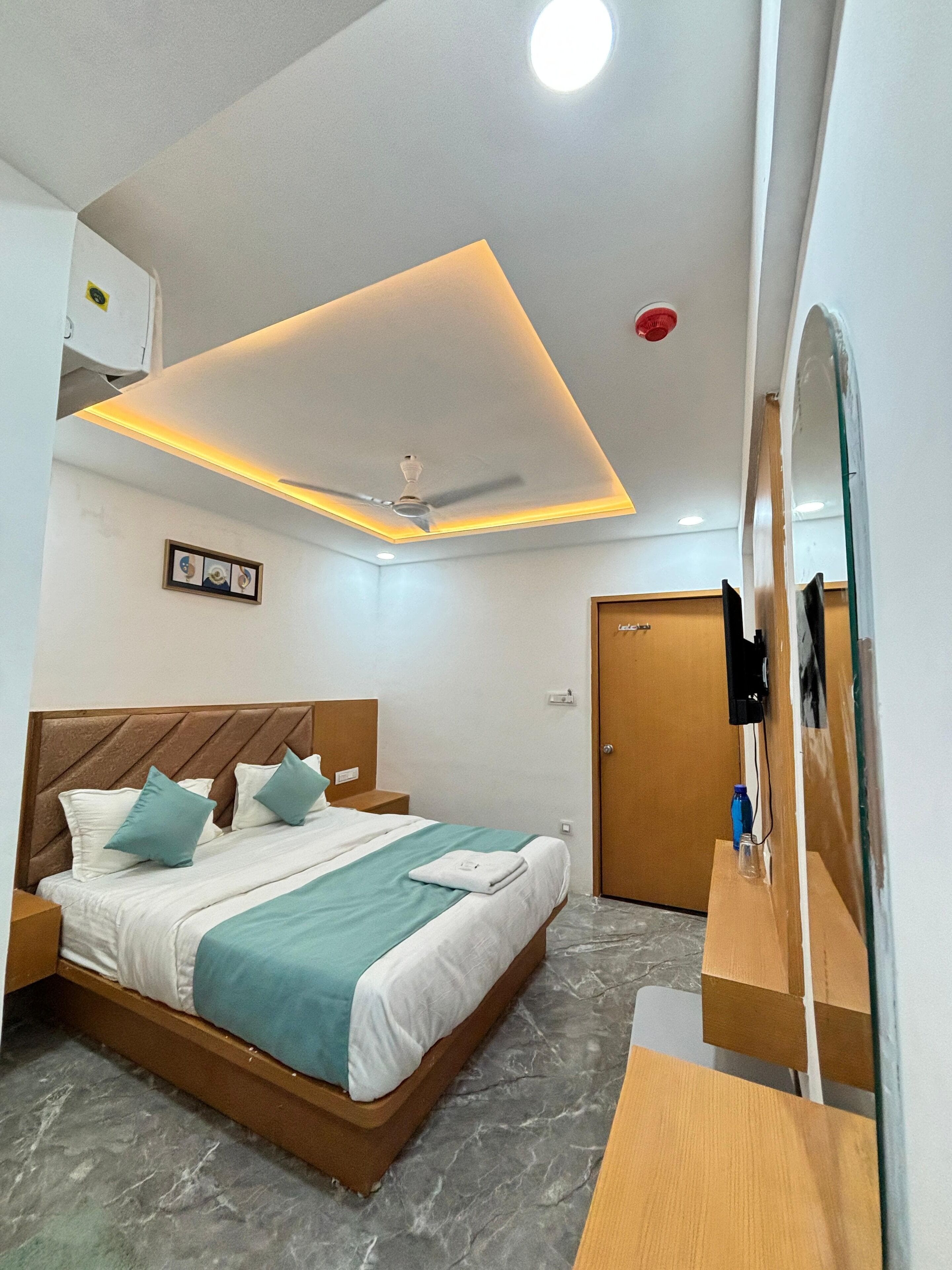 A modern hotel room with a bed, a ceiling fan, a mounted TV, and a wooden nightstand.