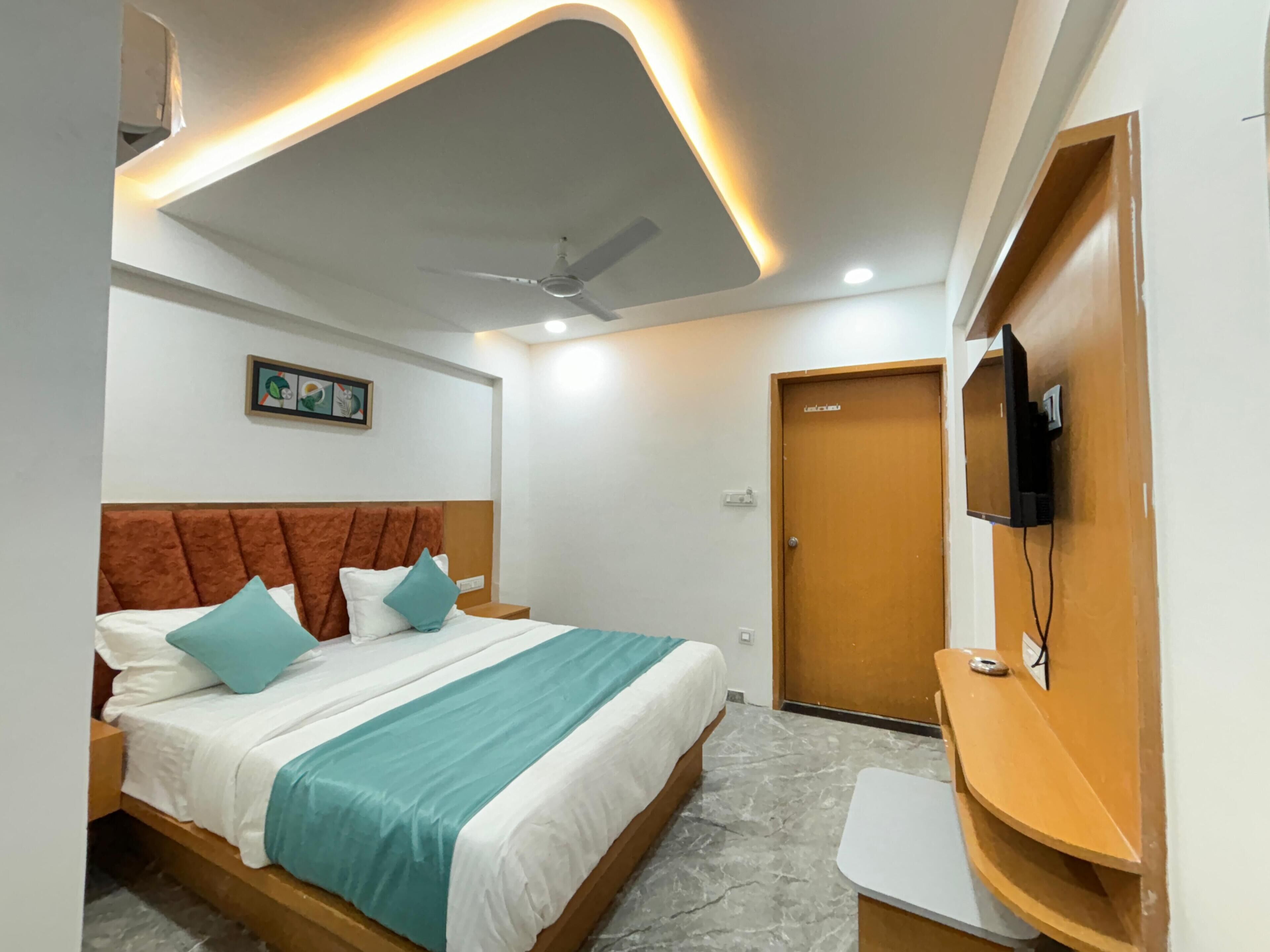 A hotel room with a bed, a ceiling fan, a TV mounted on the wall, and a wooden door.