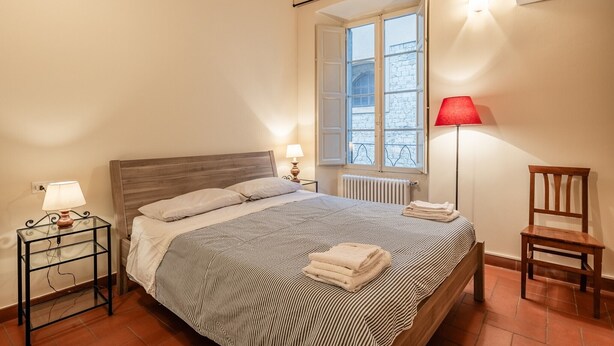 A bedroom with a bed, bedside tables, a chair, a window, and a radiator. - 'Via Abbi Pazienza Guest House' Apartment with Wi-Fi and Air Conditioning (Pistoia)