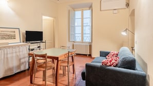 A dining area with a table and chairs, a television, a window with a view, and a sofa with a blanket. - 'Via Abbi Pazienza Guest House' Apartment with Wi-Fi and Air Conditioning (Pistoia)