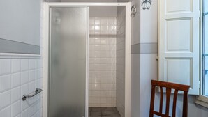 A shower with frosted glass doors, a wooden chair, and a white tiled wall. - 'Via Abbi Pazienza Guest House' Apartment with Wi-Fi and Air Conditioning (Pistoia)