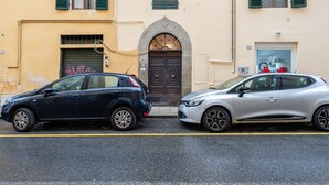 Two cars parked on a street with a building featuring a large arched entrance and green shutters. - 'Via Abbi Pazienza Guest House' Apartment with Wi-Fi and Air Conditioning (Pistoia)