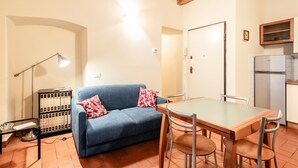 A compact living space with a sofa, dining table, chairs, a lamp, a cabinet, and a refrigerator. - 'Via Abbi Pazienza Guest House' Apartment with Wi-Fi and Air Conditioning (Pistoia)