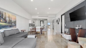 A modern living room with a large grey sofa, a small round table, and a TV mounted on the wall. - Deck 12 Vallarta Residences (Puerto Vallarta)