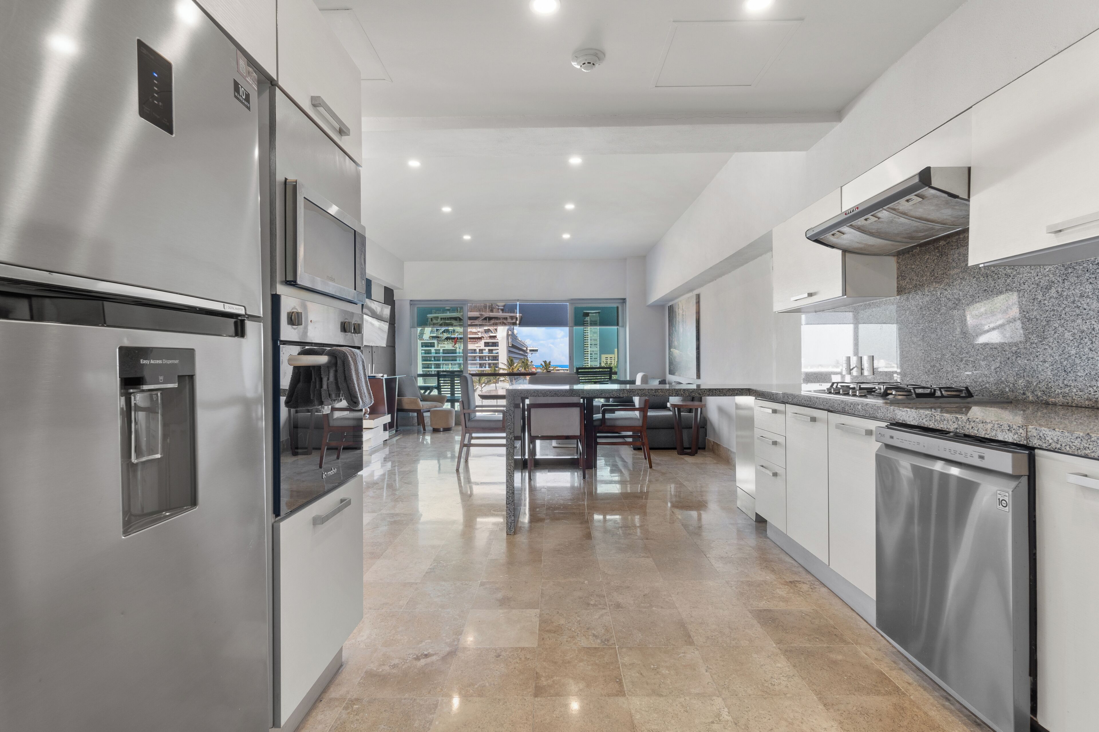 Cozinha moderna com eletrodomésticos de aço inoxidável, bancada de granito e vista para a cidade através de grandes janelas.