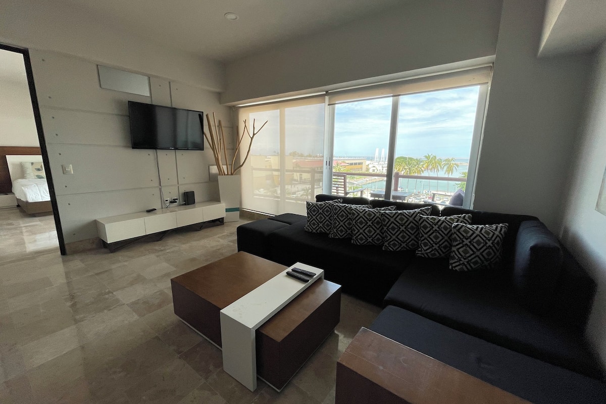 A modern living room with a black sofa, a coffee table, and a TV mounted on the wall.