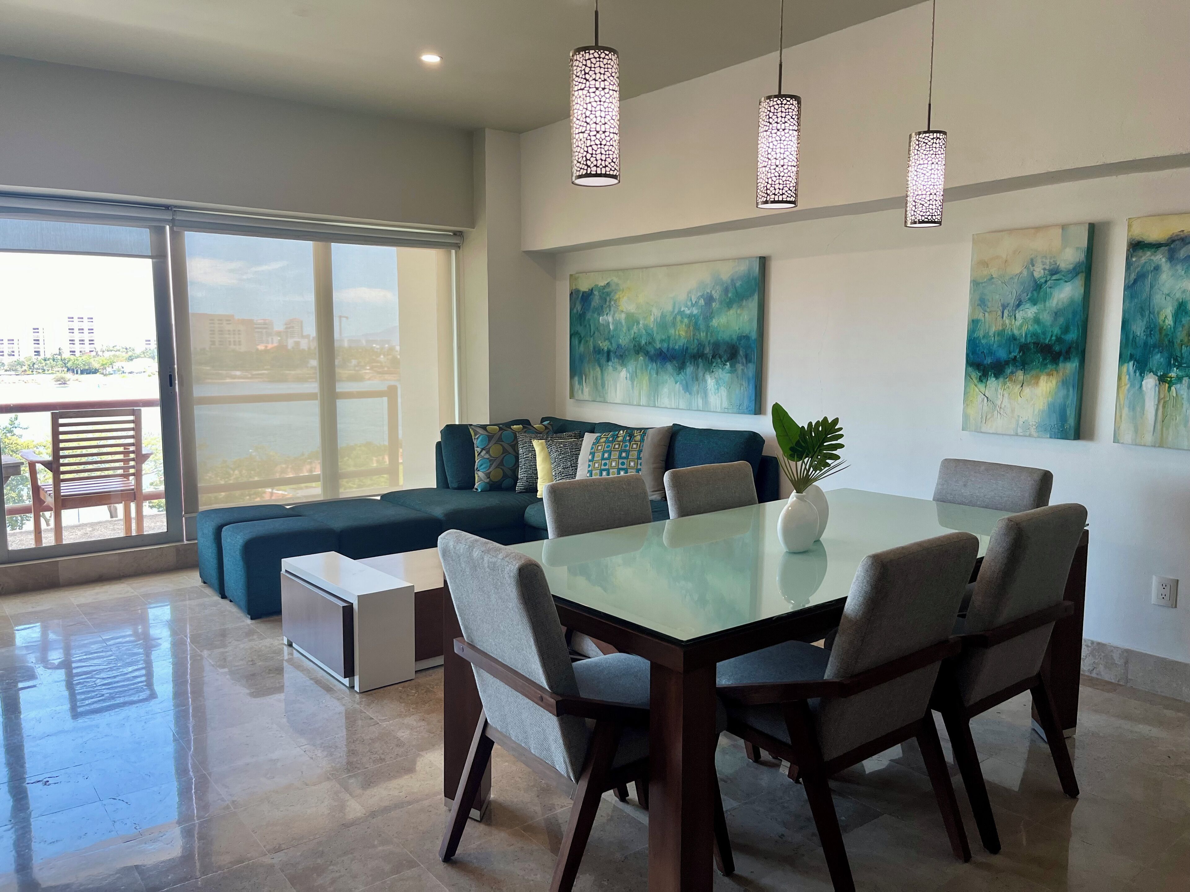 Uma sala de estar moderna com mesa de jantar de vidro, assentos confortáveis e grandes janelas com vista para a cidade.