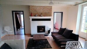 A living room with a fireplace, a sofa, a coffee table, and a white chair. - Ideal for a large family, authentic Landes house, pets welcome (Biscarrosse)