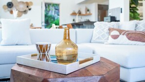 Una sala moderna con un sofá blanco, una mesa de centro de madera y un florero de vidrio decorativo.