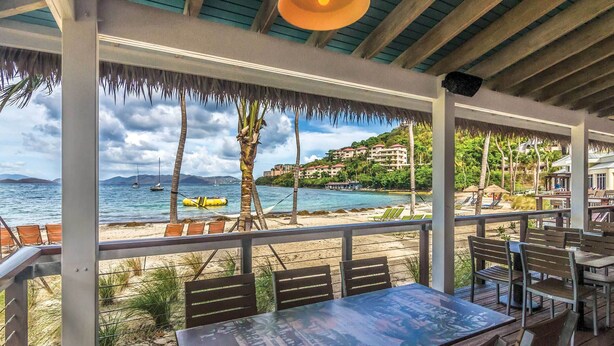 Un restaurante frente a la playa con terraza, vista al mar y techo de paja.