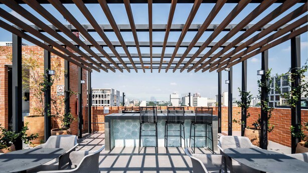 En udendørs terrasse med pergola, siddepladser og barområde med udsigt over byen.