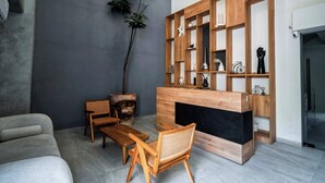 En moderne stue med sofa, sofabord i træ, stole, reoler i træ og en stor stueplante.