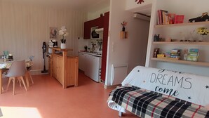 Une pièce confortable comprenant un coin repas, une kitchenette et un lit agrémenté d’un coussin aux motifs inspirants.