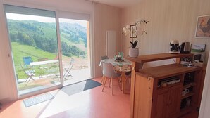 Une cuisine moderne avec un plan de travail en bois, une machine à café et une vue sur un paysage verdoyant, visible à travers une porte-fenêtre coulissante.