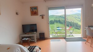 Un salon équipé d’un téléviseur, d’une petite table, d’un canapé et d’une porte-fenêtre coulissante donnant sur un balcon aménagé avec du mobilier d’extérieur.