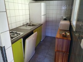 Cocina compacta con estufa a gas, pileta y refrigerador blanco.