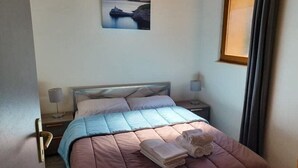 A neatly made bed with a pink and blue bedspread, two pillows, and two folded towels on a wooden nightstand with a lamp. - casa del torrent (Ota)