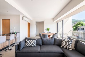 A modern living area with a sofa, dining table, and chairs, a kitchen with bar stools, and a balcony with a view. - Cozy Downtown Apartment Perfect for Couples (Puerto Vallarta)