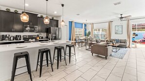 A modern kitchen with dark cabinets, a white countertop, and a central island with stools. - Be our guest At Championsgate (Davenport)