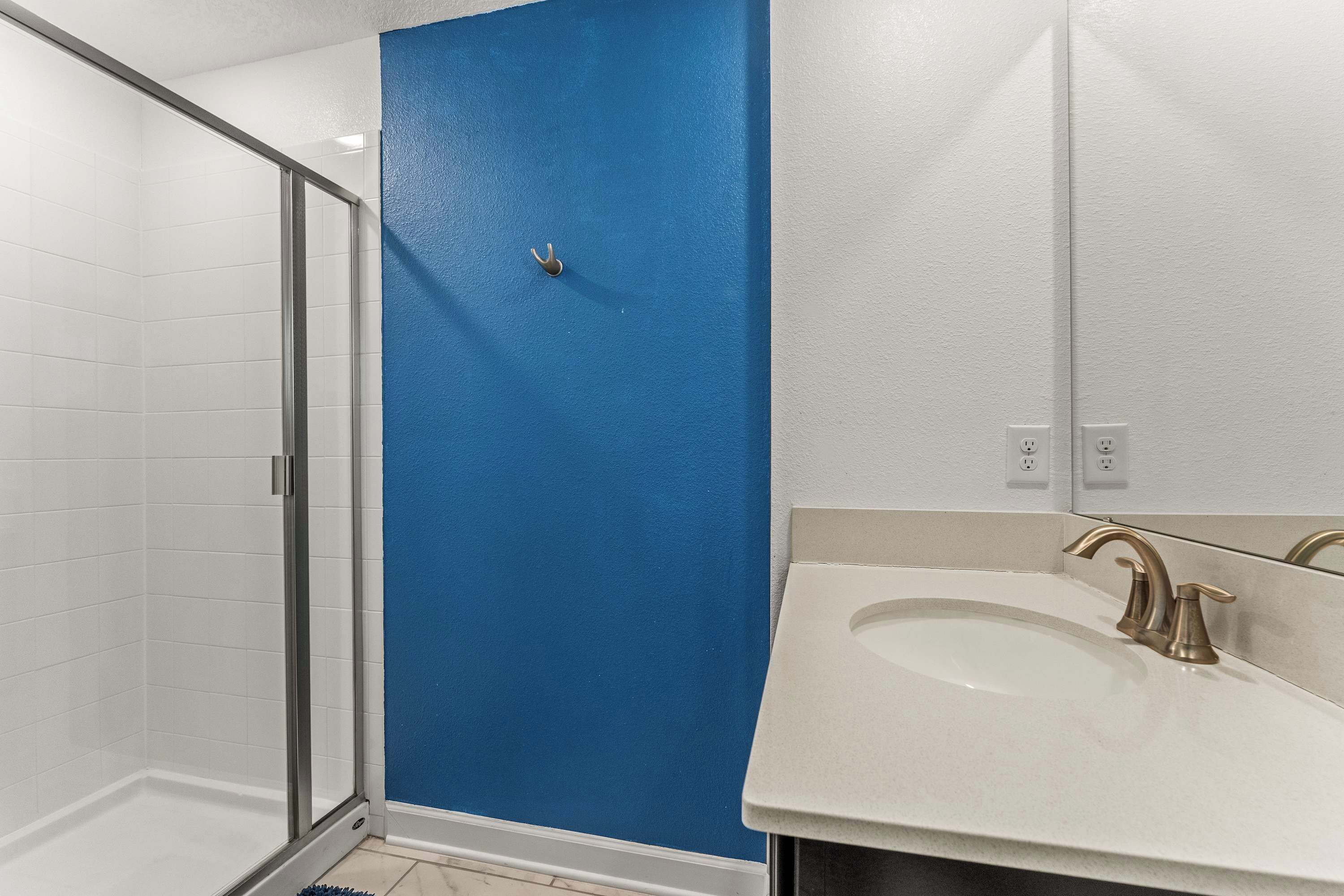 A bathroom with a glass shower enclosure, a blue door, and a white sink with a gold faucet.