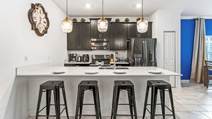 A modern kitchen with a central island, black bar stools, and pendant lighting. - Be our guest At Championsgate (Davenport)