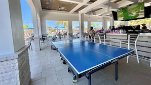An indoor pool area with a ping pong table, seating, and a bar area with a TV. - Be our guest At Championsgate (Davenport)