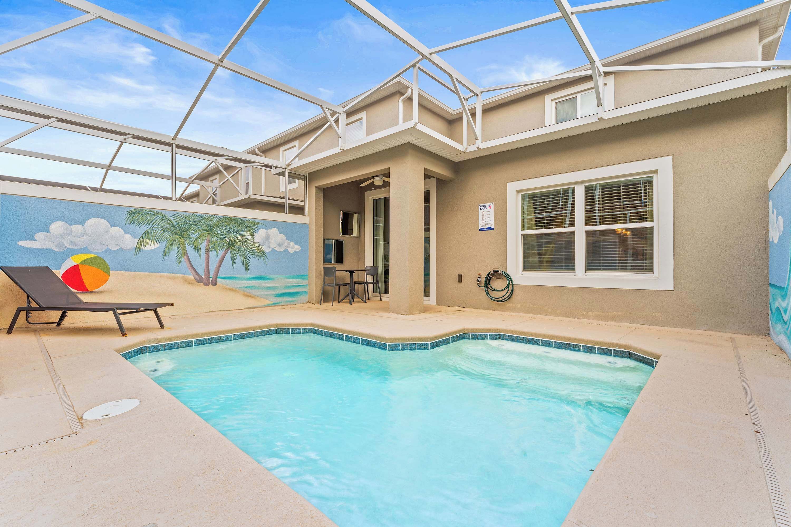 An indoor swimming pool with a beach mural, lounge chairs, and a covered patio area.